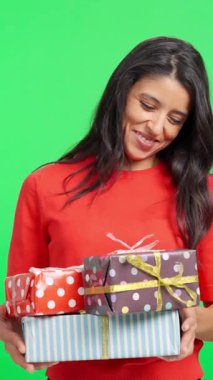 Gülümseyen kadın yeşil perde arkasında bir yığın Noel hediyesi tutuyor.