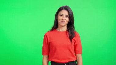 Kollarını kavuşturmuş genç bir iş kadını yeşil perde arkasında güvenle gülümsüyor.