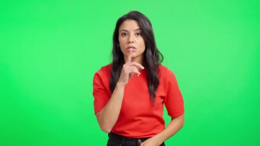 Genç İspanyol bir kadın yeşil ekranda dudaklarında bir parmakla sessizlik için el sallıyor.