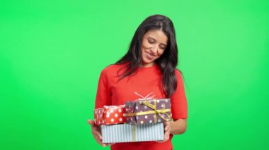 Gülümseyen kadın yeşil perde arkasında bir yığın Noel hediyesi tutuyor.