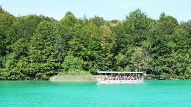 Hırvatistan 'ın Plitvice Gölleri' nin kristal berrak turkuaz suyunda turist taşıyan elektrikli tekne
