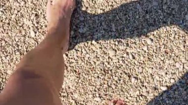 Bir kadının ayaklarının güneşli bir çakıl taşlı plajda dalgalarla ıslanmasının yavaş çekim bakış açısı