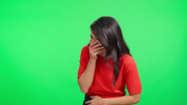 Genç Latin bir kadın yeşil ekran arkasında dururken kontrolsüz bir şekilde gülüyor.