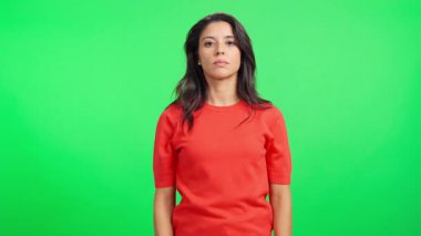 Genç, ciddi bir kadın yeşil ekranda kızgın ve hayal kırıklığına uğramış bir ifadeyle kollarını kavuşturuyor.