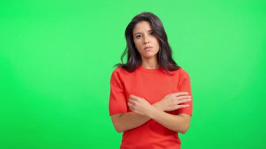Ciddi ve sinirli bir kadın yeşil ekran arka planında ifade edici bir yüzle kollarını kavuşturuyor.