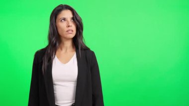 Siyah ceketli rahatsız bir iş kadını yeşil arka planda bir şeyler okuyor.