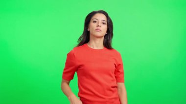 Yüzünde ciddi bir ifade olan beyaz kadın elini yeşil ekran arka planında gezdirip duruyor.