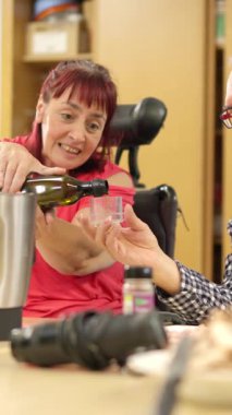 Tekerlekli sandalyede sakat gülümseyen bir kadın yemek pişirirken bir erkeğe zeytinyağı döküyor.