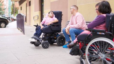 Çeşitli arkadaşlar, tekerlekli sandalyeler, kaldırımda sohbet etmek.