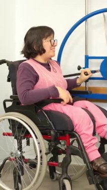 Tekerlekli sandalyedeki beyaz kadın spor salonunda fiziksel rehabilitasyon için kol egzersizi yapıyor.