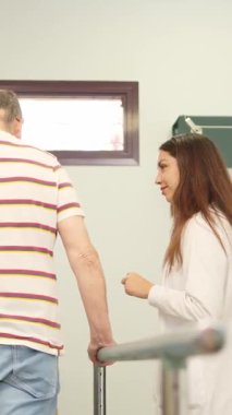 Engelli bir adam, kadın bir doktorla fizik tedavi egzersizleri için paralel çubuklar kullanıyor.