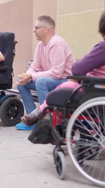 İki adam ve fiziksel engelli bir kadın bir caddede dostça sohbet ediyorlar.