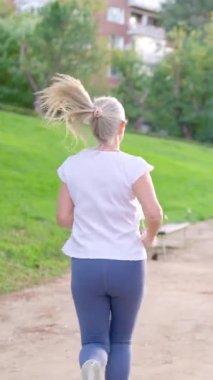 Sarı at kuyruklu yaşlı bir kadın gün boyunca parkta pis bir yolda koşuyor.