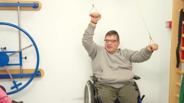 Tekerlekli sandalyedeki adam rehabilitasyon için fizik tedavi seansında kollarını çalıştırıyor.