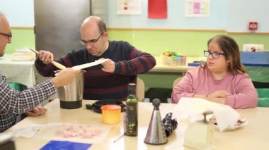 Fiziksel engelli bir adam mutfakta yemek pişirirken arkadaşıyla iş birliği yapıyor.