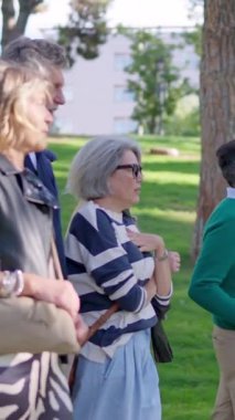 Bir grup mutlu, olgun, gri saçlı arkadaş güneşli bir parkta konuşuyor ve birlikte yürüyorlar.