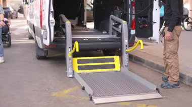 Tekerlekli sandalyedeki bir adam, şehir caddesinde otomatik asansörle ulaşılabilir bir minibüsten çıkıyor.
