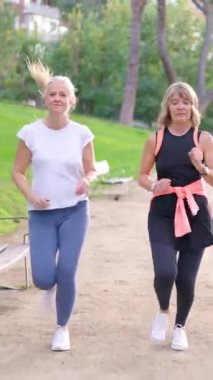 İki olgun bayan arkadaş parkta ağır çekimde antrenman yapmak için birlikte koşuyorlar.