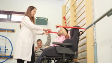 Fiziksel engelli genç bir adam rehabilitasyon egzersizleri yapıyor. Kadın bir terapistin yardımıyla.