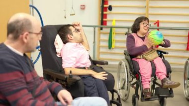 Fiziksel engelli bir grup yetişkin rehabilitasyon merkezinde top atarken eğleniyor.