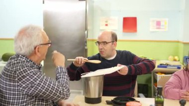 Engelli iki adam yemek pişirme dersinde iş birliği yapıp yemek tarifi hazırlıyorlar.