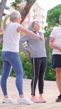 Spor giyim sektöründe aktif kıdemli insanlar şehir parkında spor yaparken kaslarını esnetiyorlar.