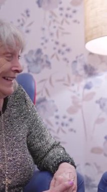 Mutlu, yaşlı bir büyükannenin mavi bir koltukta yavaşça otururken gülüşünü yakından çek.