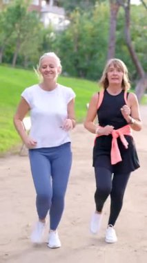 İki olgun kadın parkta koşmaktan zevk alıyor, gülümsüyor ve aktif kalıyorlar.