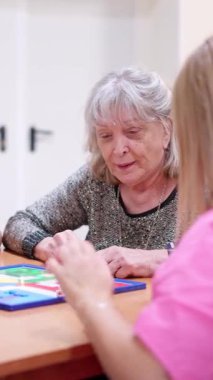 Yaşlı kadın ve hemşire bilişsel terapi için bakımevinde masa oyunu oynuyorlar.