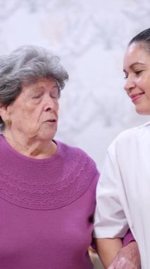 Yaşlı bir kadını destekleyen nazik kadın hemşire, huzurevinde yardım ve bakım sunuyor.