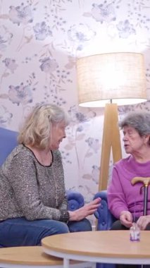 Yaşlı annesini huzurevinde ziyaret eden bir kız. Gülümseyen bir bakıcı ise onlara yardım ediyor.