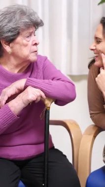 Yaşlı bir kadın elinde bastonla oturuyor ve torunuyla gülüyor.