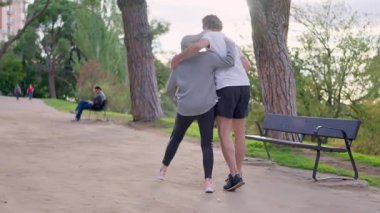 Olgun, beyaz bir çift, güneşli bir günde parkta neşeyle dans ediyor.