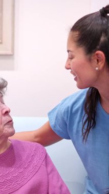 Genç bir kadın, büyükannesini bir bakımevinde sevgiyle ziyaret eder, konuşur ve onu rahatlatır.