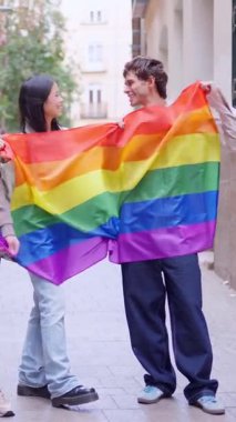 Mutlu çift gurur ayını gökkuşağı bayrağıyla kutluyor ve şehirde gülümsüyor.