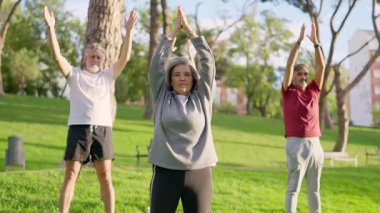 Bir grup aktif son sınıf öğrencisi güneşli bir günde açık havada yoga ve esneme egzersizleri yapıyor.