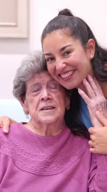 Genç bir kadının gülümseyerek yaşlı büyükannesine sarılmasının şefkatli anı.