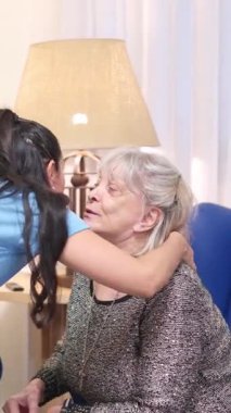 Genç bir kadın huzurevinde gülümseyen yaşlı büyükannesine şefkatle sarılıp öpüyor.