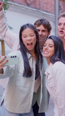 Mutlu çok ırklı arkadaş grubu akıllı telefonuyla selfie çekiyor ve birlikte komik suratlar yapıyorlar.