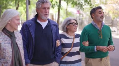 Bir grup şık olgun arkadaş sokakta gülerek ve konuşarak yürüyüş yapıyorlar.