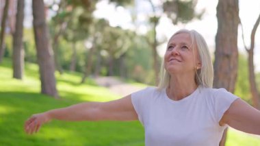 Gri saçlı, mutlu, olgun bir kadın. Parkın sakinliğinin tadını çıkarıyor ve derin nefes alıyor.
