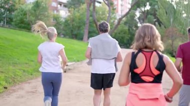 Yeşil bir şehir parkında, toprak yolda birlikte koşan yaşlı insanların arka görünüşü.