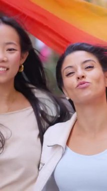 Gurur ve aşkı kutlayan iki neşeli genç kadın şehir sokaklarında renkli bir bayrak ile