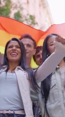 Eşcinsel onur yürüyüşü sırasında ellerinde gökkuşağı bayrağı tutan bir grup mutlu çok ırklı arkadaş.