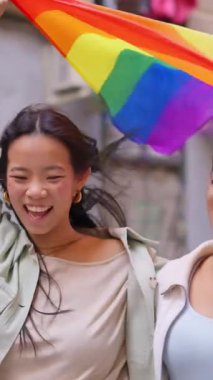 Gurur yürüyüşü sırasında gökkuşağı bayrağı sallayan çok ırklı genç lezbiyen çift