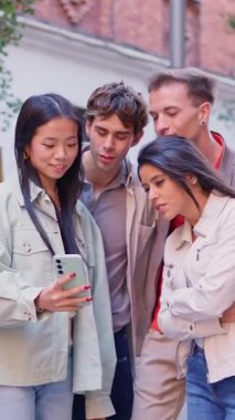 Çok ırklı bir arkadaş grubu açık havada gülümserken akıllı telefondan bir şey izliyor.