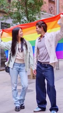 Gülümseyen çok kültürlü bir adam ve kadın şehrin sokaklarında yürürken gururlu bir bayrak tutuyorlar.