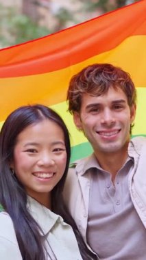 Mutlu Asyalı bir kadın ve beyaz bir adam gururlu bir bayrağa sarılmış gülümsüyor.