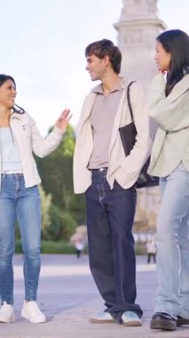 Üç etnik çeşitlilikte genç arkadaş bir kentin dışında bir arada durup konuşuyor ve gülümsüyor.