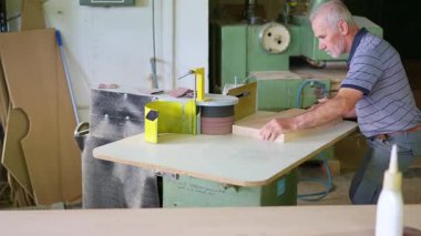 Eski profesyonel marangoz marangozluk atölyesinde zımpara makinesiyle ahşap bir yüzeyi düzleştiriyor.